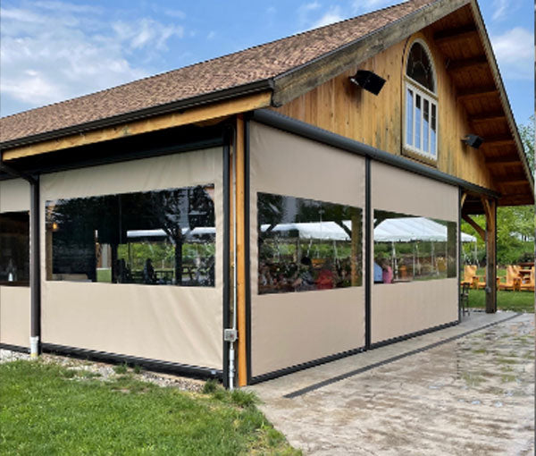 The covered porch of a timber building enclosed with beige and clear vinyl weather screens.