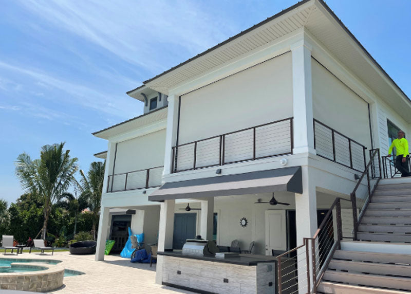 A two-storey home with motorized screens lowered across an upper balcony and the covered patio below it.